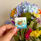 Hand holding the mini capybara pin under natural lighting