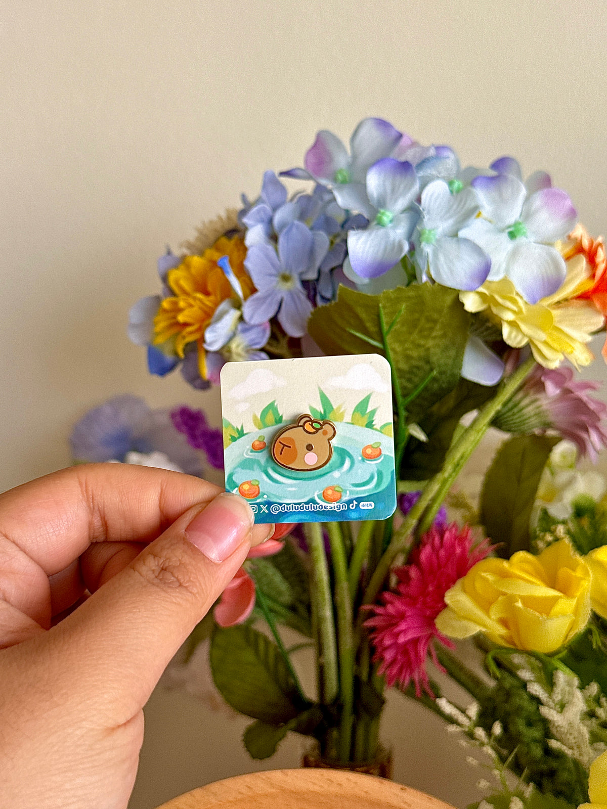 Hand holding the mini capybara pin under natural lighting