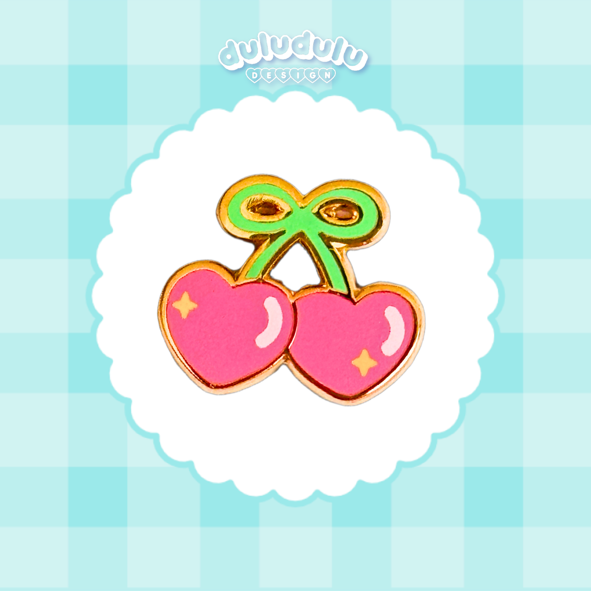 A cute enamel pin shaped like two pink heart-shaped cherries with a green bow on a scalloped white background. 