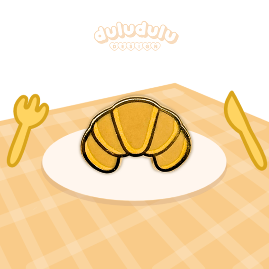 A croissant pin on a white plate, set on a yellow-orange checkered tablecloth.