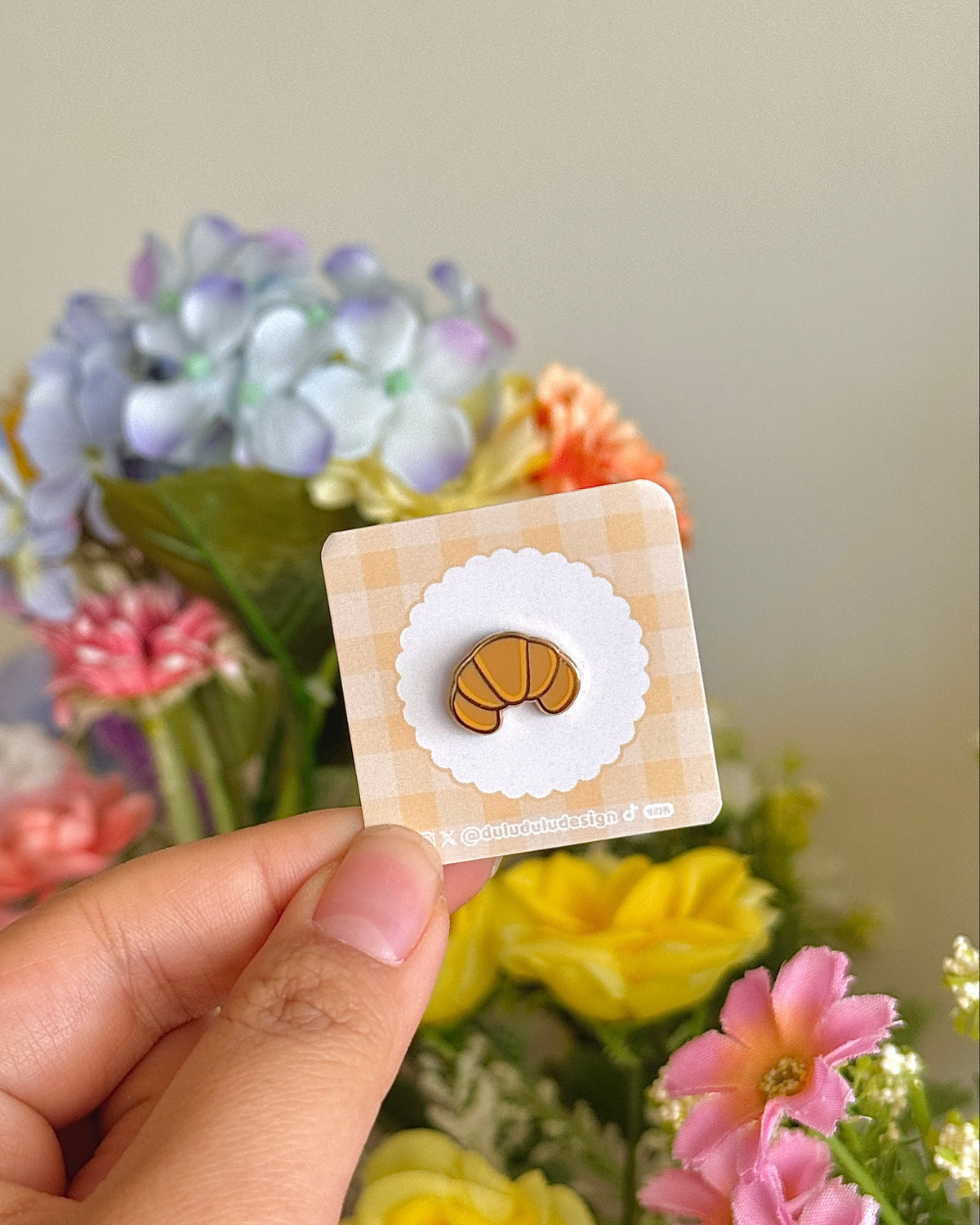 Hand holding croissant mini pin under natural lighting