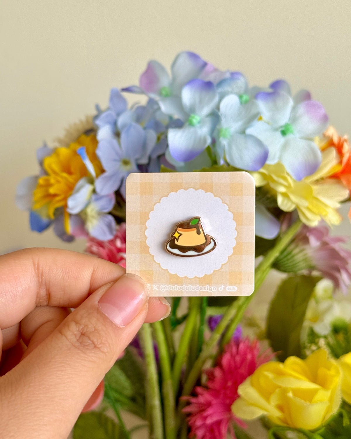 hand holding flan mini enamel pin under natural sunlight