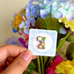 Hand holding a flower mini pin under natural sunlight