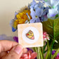 hand holding fruit crepe mini enamel pin under natural sunlight