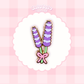 A lavender bouquet enamel pin displayed on a white scalloped circle over a pink checkered background.