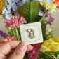 hand holding lily of the valley mini pin under natural lighting
