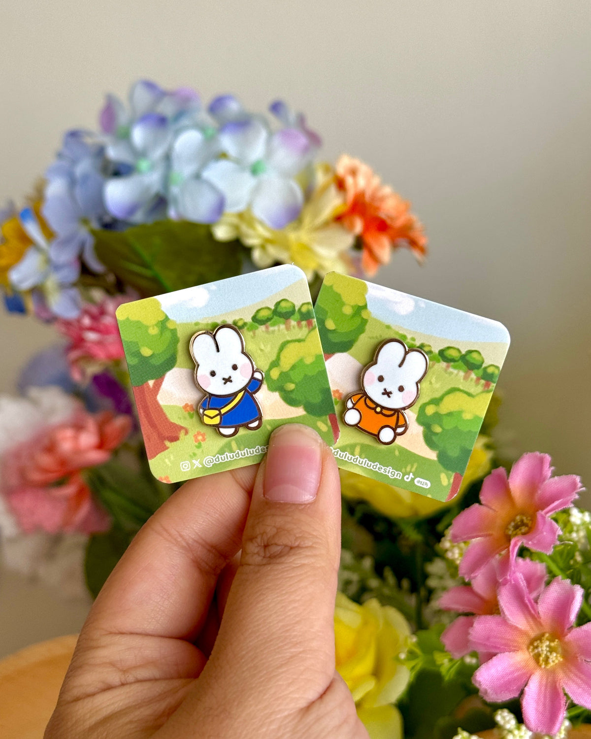 hand holding 2 miffy enamel pins under natural lighting