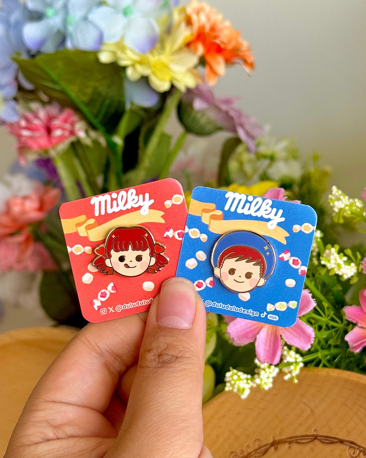 Hand holding peko and poko character mini pins under natural light