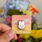 a hand holding on mute rabbit enamel pin under natural sunlight