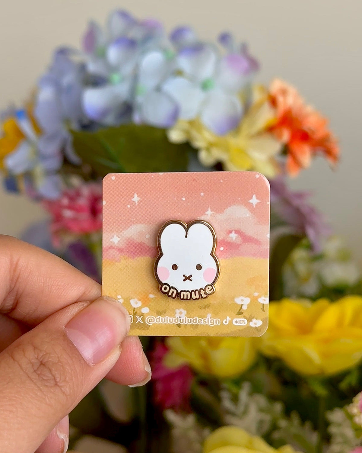 a hand holding on mute rabbit enamel pin under natural sunlight