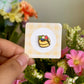 Hand holding fruit pancake mini enamel pin against floral background