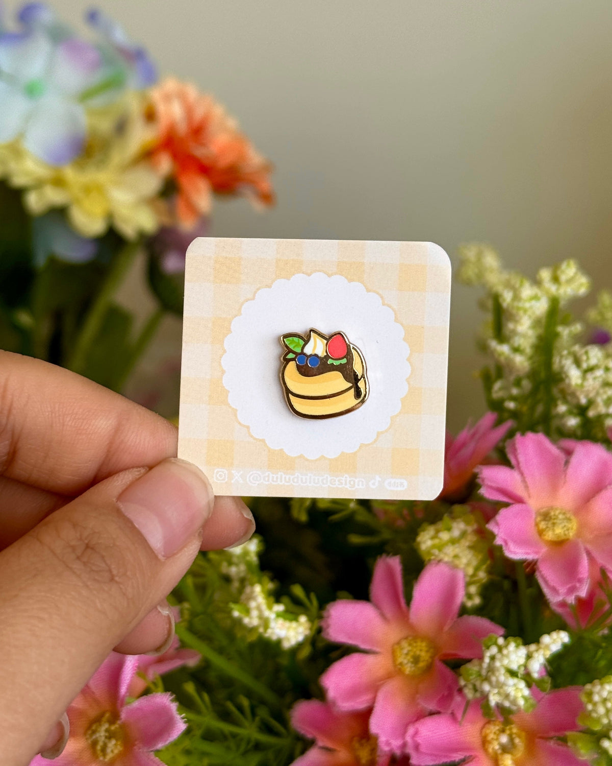 Hand holding fruit pancake mini enamel pin against floral background