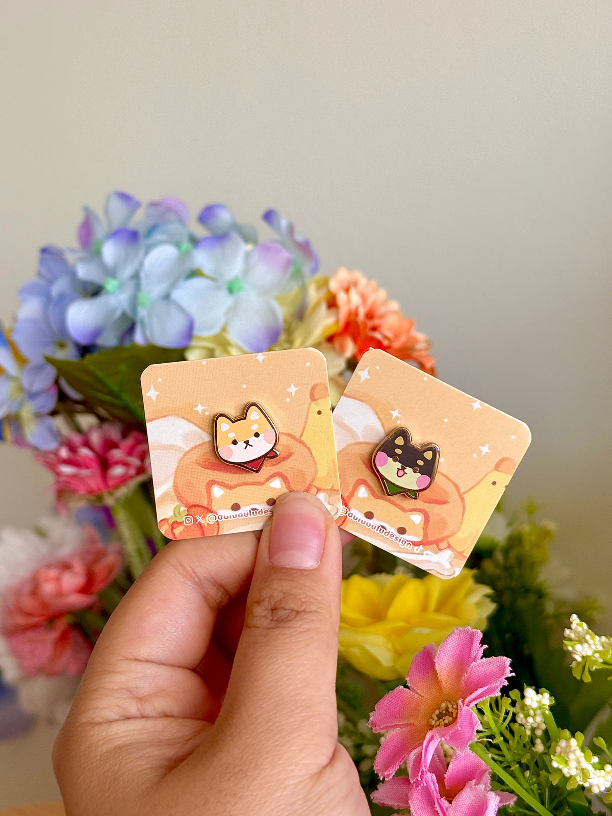 Hand holding both shiba inu pins under natural lighting